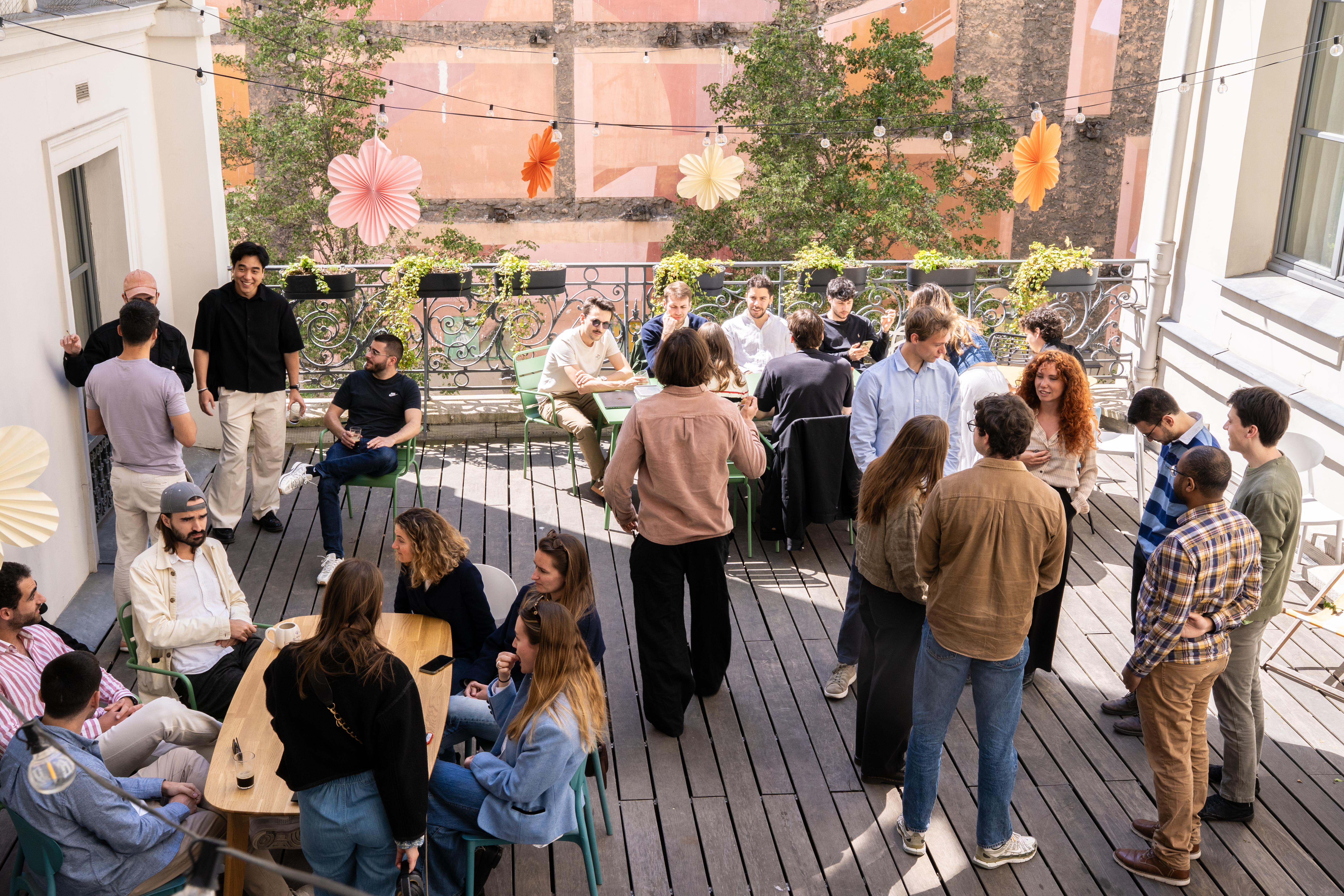 Une trentaine de Galadrimeurs discutent et se détendent sur la terrasse en bois des bureaux, décorée de fleurs en papier.