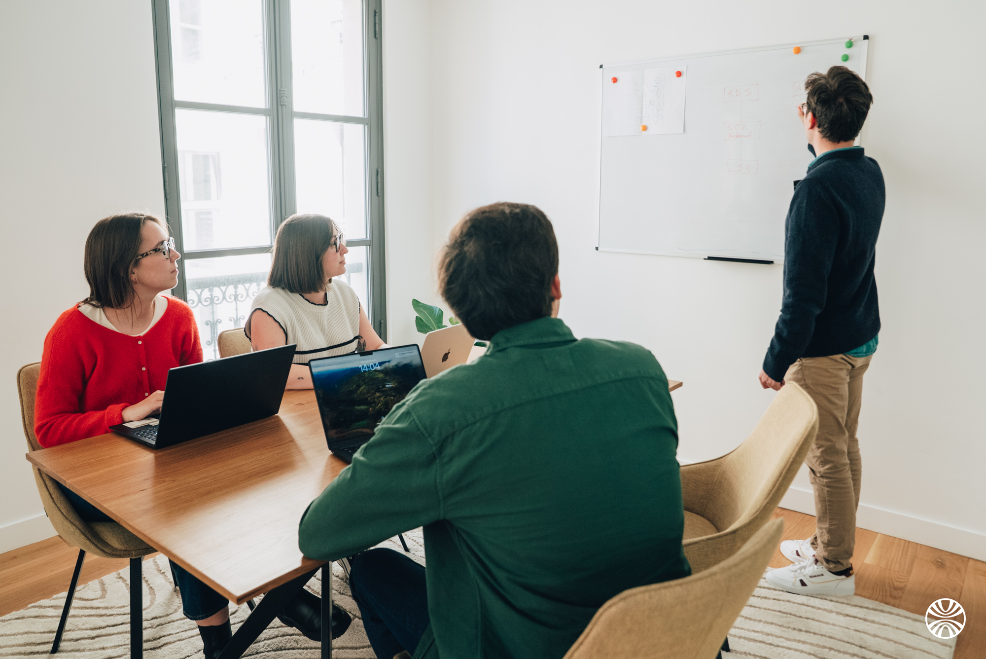 Une équipe autour d'une table avec des ordinateurs portables écoute une personne au tableau blanc